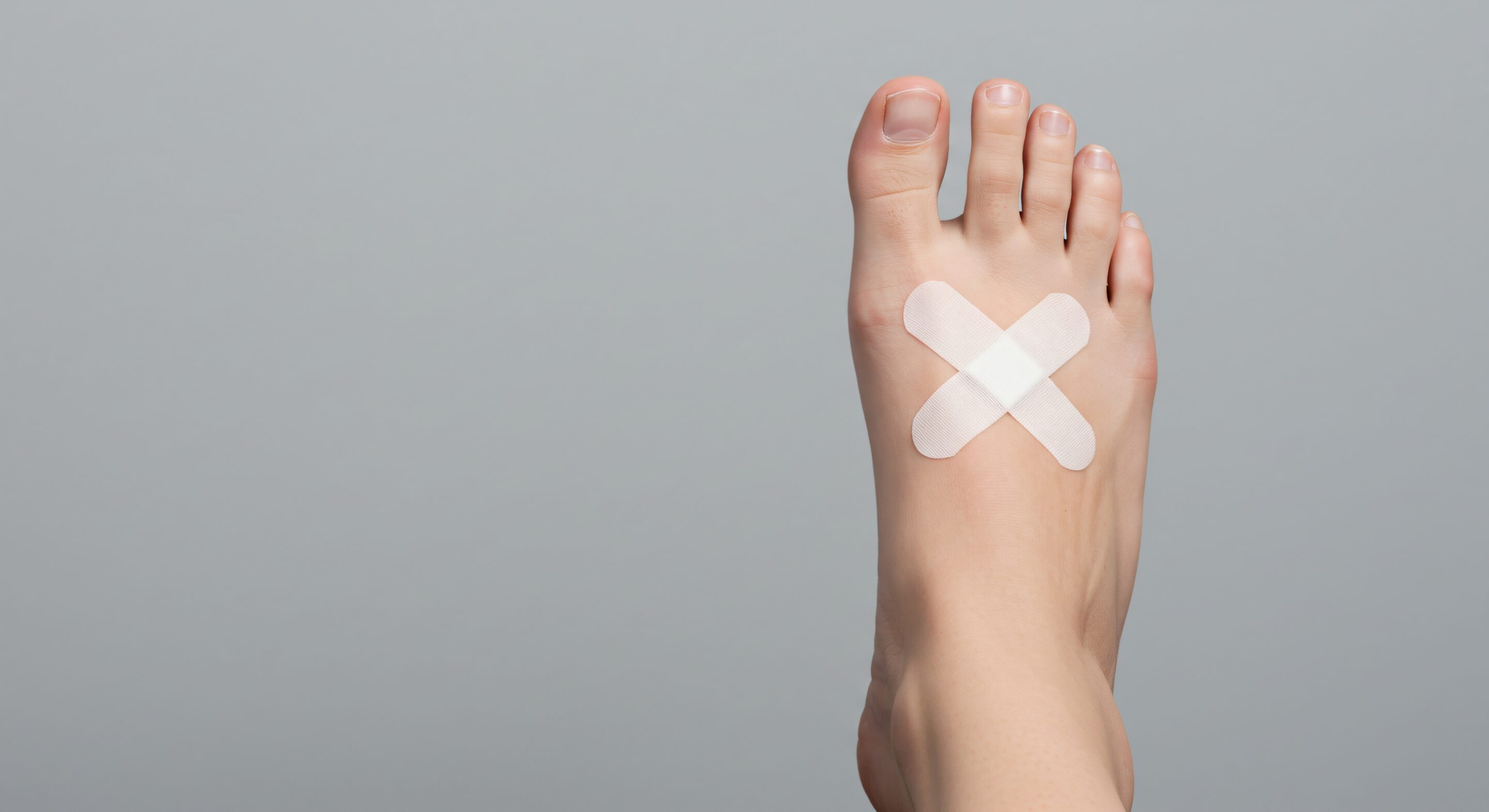 A caucasian woman's foot with two crossed beige adhesive bandages on the top. Foot injury and wound protection concept.